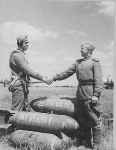 two men shaking hands in front of tanks with words written on the tank and another man standing next to them