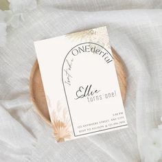 a wooden plate with a card on it sitting on a white cloth covered tablecloth