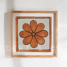 an orange and white flower is in a wooden frame on the wall next to a plant