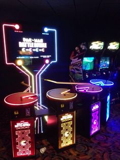 several video game machines are lit up in the dark with neon signs on each side