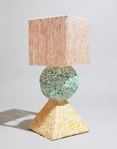 a lamp that is sitting on top of a small base with a pink and green shade