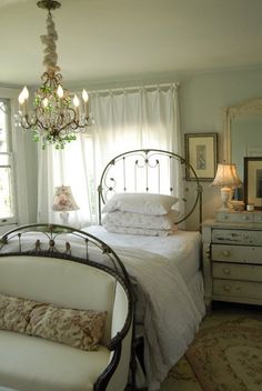 a white bed sitting next to a window in a bedroom under a chandelier