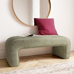 a green bench sitting in front of a mirror on top of a wooden floor next to a rug