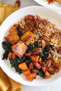 a white bowl filled with rice, carrots and tofu on top of greens