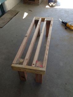 a wooden bench sitting on top of a cement floor next to a building with tools