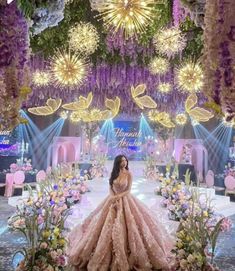 a woman standing in front of a stage decorated with flowers and lights, wearing a pink gown