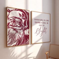 two framed christmas cards hang on the wall next to a chair and window with sunlight coming in