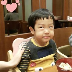 a little boy sitting in a high chair with food on the table next to him