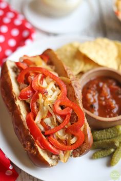 a white plate topped with a hot dog covered in toppings next to green beans and tortilla chips