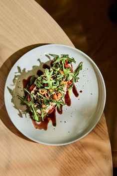 a white plate topped with vegetables and sauce on top of a wooden table next to a cup