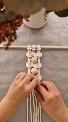 a woman is working on a piece of art with white yarn and wood beading