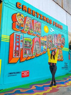 a woman standing in front of a mural on the side of a building that says san francisco