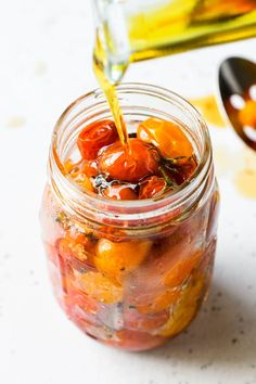 a glass jar filled with tomatoes and olives being drizzled with oil