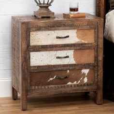 a nightstand with two drawers and a cow hide on the bottom shelf next to a bed