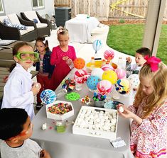 a group of children standing around a table filled with cake and desserts at a birthday party