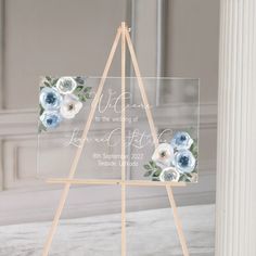 a clear acrylic sign with blue and white flowers on it in front of a marble floor