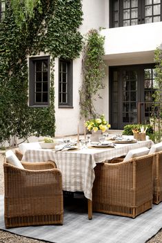 an outdoor table with two chairs and a table cloth on it, in front of a house