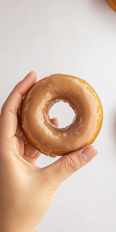 a person holding a glazed donut in their hand next to some doughnuts