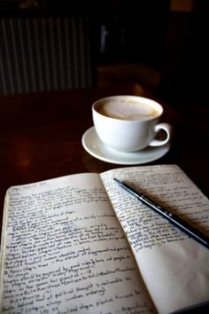 an open book with writing on it next to a cup of coffee and a pen