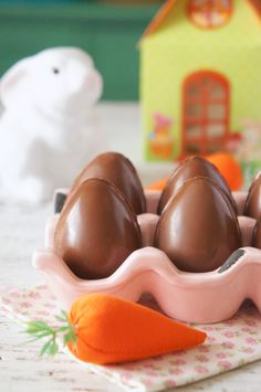 some chocolate eggs are in a pink egg carton with an orange carrot on the side