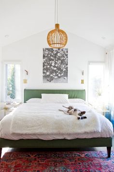 a dog laying on top of a white bed in a room with lots of windows