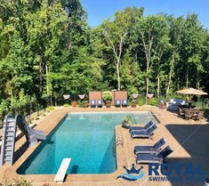 an empty swimming pool surrounded by lounge chairs and umbrellas with trees in the background