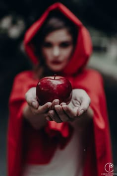 a woman in a red cloak holding an apple with both hands and wearing a hood