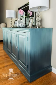 the sideboard is painted blue and has flowers in vases on top of it