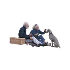 three people sitting on the ground with a dog and one is holding something in his hand