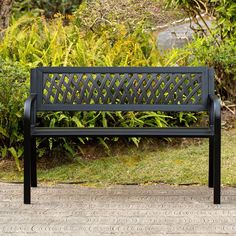 a black bench sitting on top of a brick walkway next to bushes and trees in the background