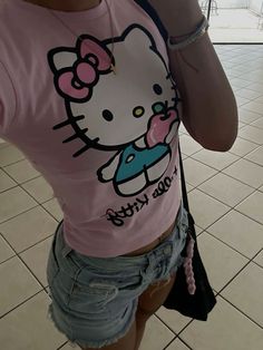 a woman taking a selfie while wearing a hello kitty t - shirt and denim shorts