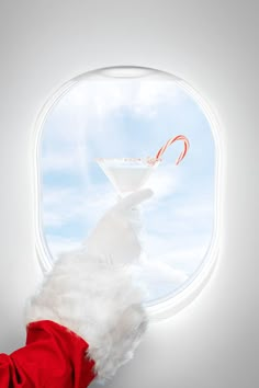 a hand holding a drink in front of an airplane window with a candy cane sticking out of it