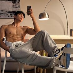 a shirtless man sitting in a chair taking a selfie with his cell phone