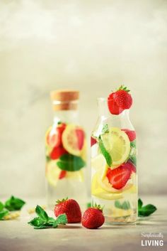 two glass bottles filled with lemon, strawberries and lime slices next to each other