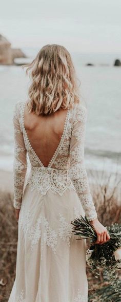 the back of a woman's dress as she walks along the beach with her bouquet in hand