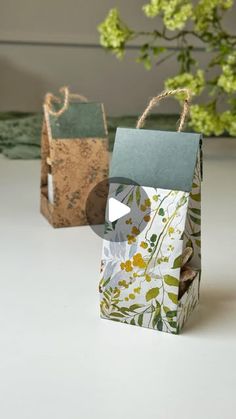 two small bags with handles are sitting next to each other on a white table and flowers in the background