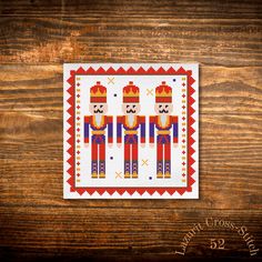 a cross stitch pattern with three men in red, blue and yellow colors on a wooden surface