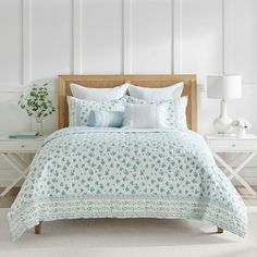 a bed with blue and white flowers on it in a room next to two lamps