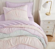 a bed with pink and white comforters in a bedroom next to a night stand