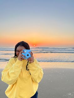 a woman taking a photo on the beach at sunset with her camera in front of her face