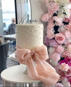 a white cake with pink flowers and a name on it sitting on a table next to a wall