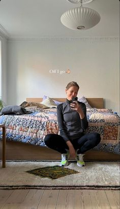 a woman sitting on the floor in front of a bed looking at her cell phone