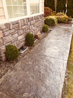 a house with stone walls and landscaping in front of the door, along side a driveway