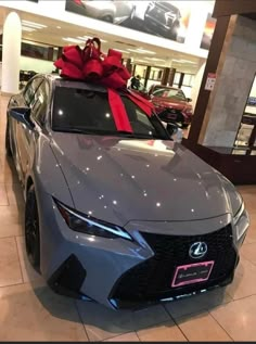 a gray car with a red bow on the hood in a showroom filled with cars