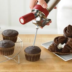 a cupcake being frosted with chocolate frosting by a hand mixer on a wire rack