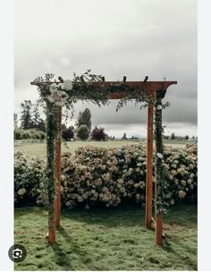 a wooden arbor with flowers and greenery on the top is in front of a hedge