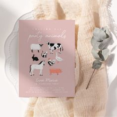 a pink card with farm animals on it next to a white plate and eucalyptus plant