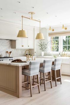 a kitchen with white cabinets and gold pendant lights hanging from the ceiling, along with four bar stools