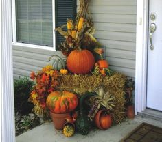 pumpkins and gourds are stacked on top of hay in front of a house