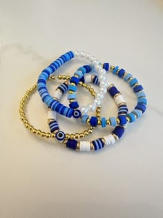 Blue and gold clay bead bracelet collection. Clay Bracelet Color Ideas, Navy Blue Clay Bead Bracelets, Beaded Jewelry Clay Beads, Cute Clay Beaded Bracelets, Cute Bracelet Clay Bead Idea, Cute Ideas For Clay Bead Bracelets, Beaded Clay Bracelets, Gold Evil Eye Bracelet With Letter And Round Beads, Fun Clay Bead Bracelet Ideas